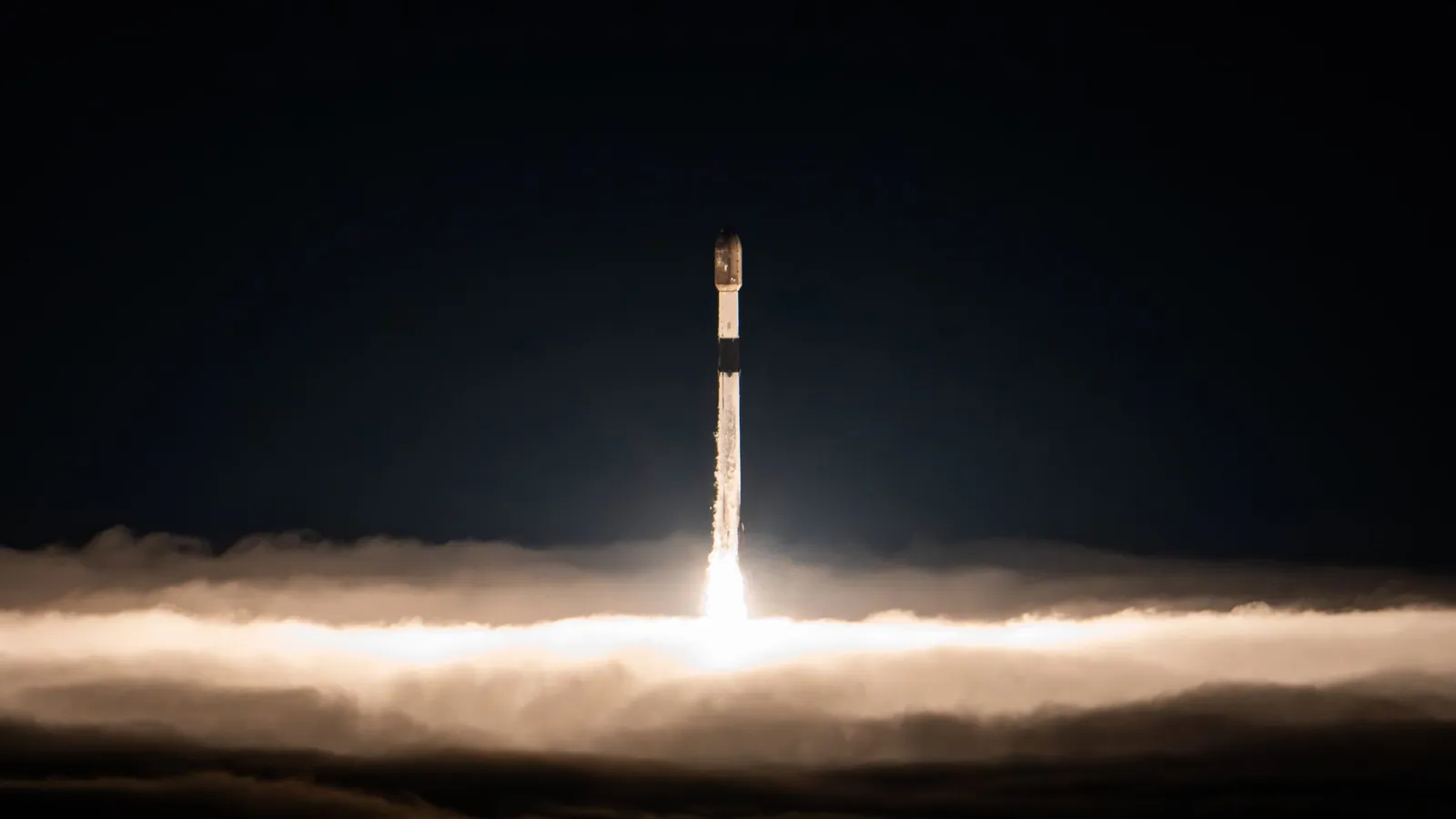 a black and white rocket rises above clouds into a dark night sky
