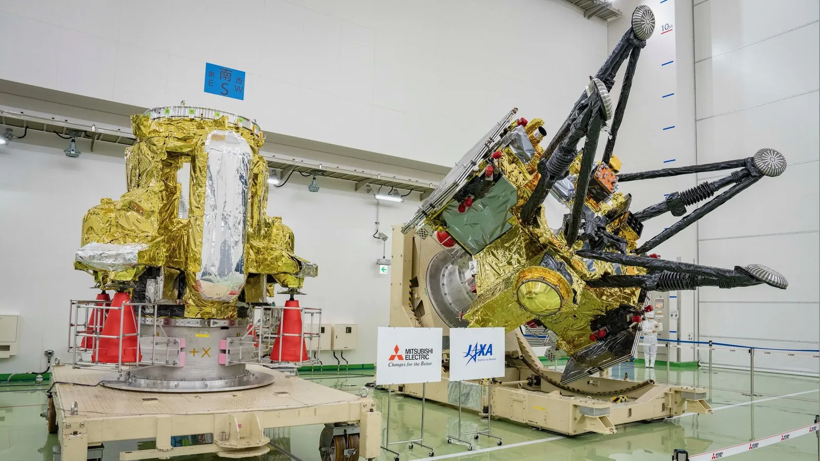 two large, gold-foil-wrapped spacecraft sit inside a large white-walled cleanroom