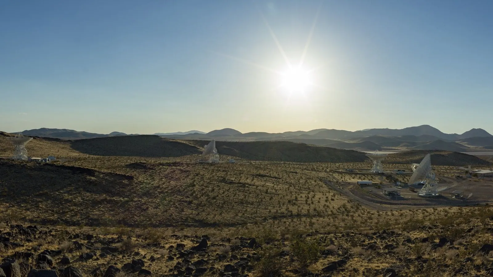 several antennas sit under a blue sky and blazing sun.