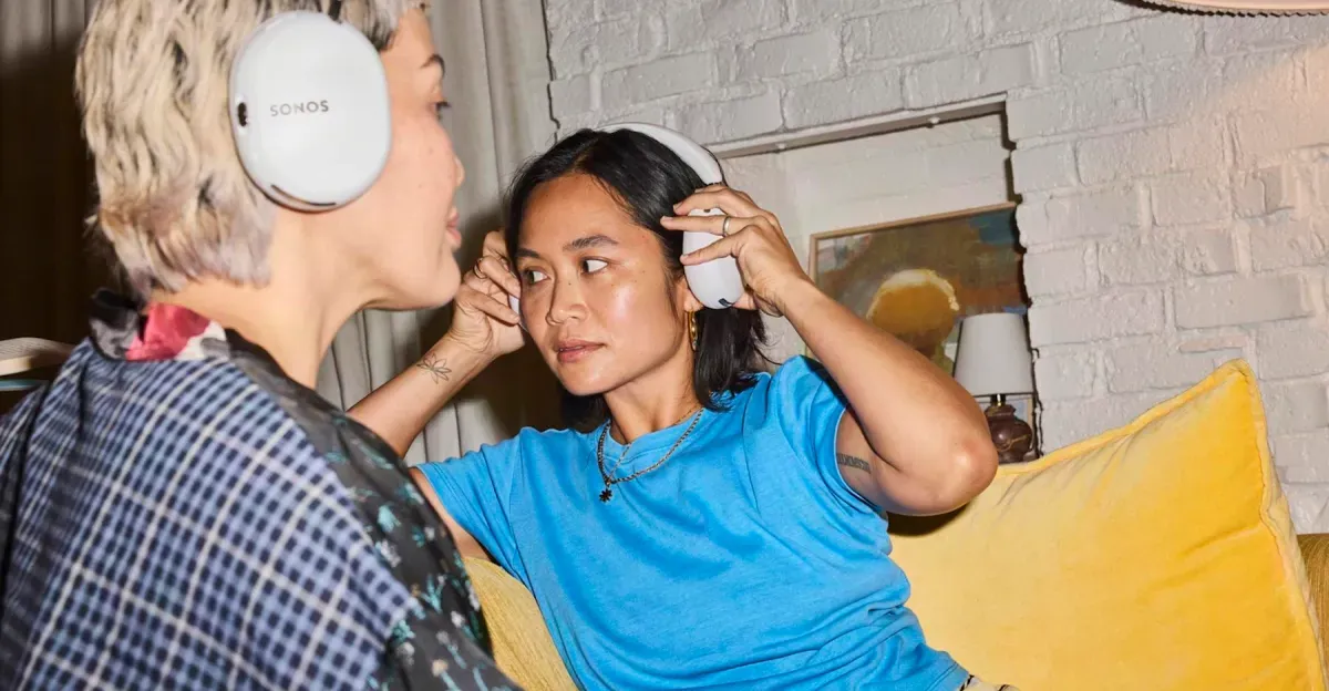 Two people sitting on a couch wearing the Sonos Ace Ultra headphones.